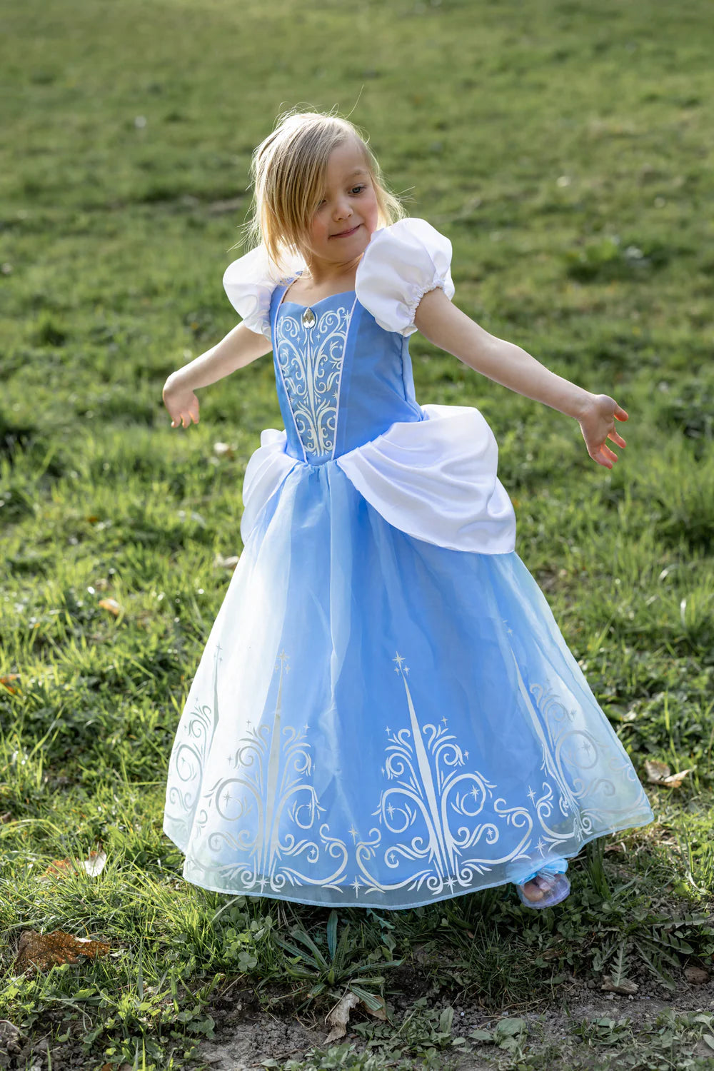 Child in a blue CINDERELLA dress with white embroidery standing on grass