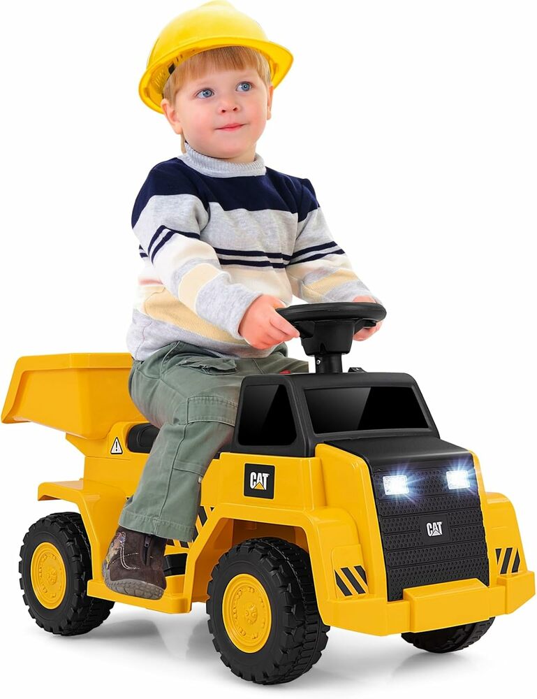 A child sitting on a yellow and black Caterpillar branded ride-on dump truck toy, wearing a hard hat.