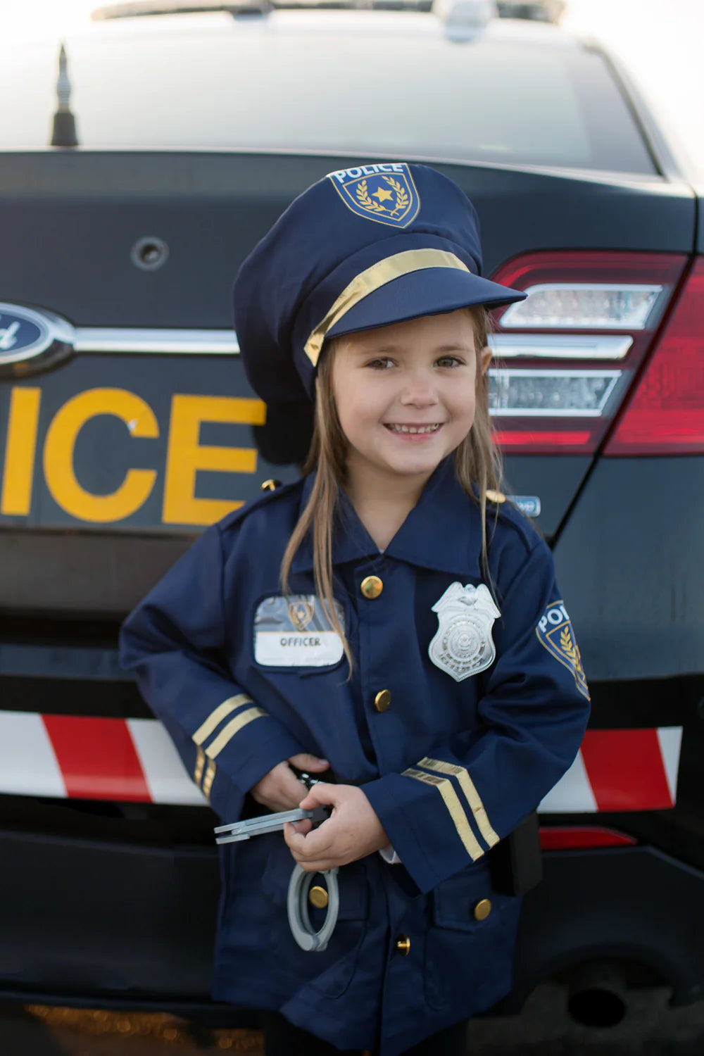 Child in a police uniform standing in front of a police car
