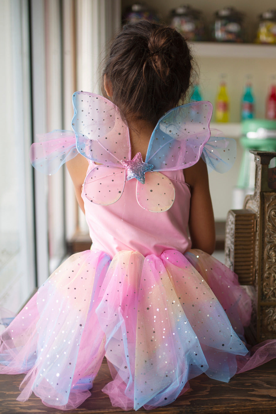 Image shows backside of costume. It features sparkly fairy wings with a star in the center. The skirt shimmers and is very colorful.