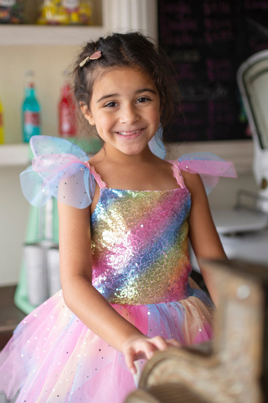 Image of young girl smiling in rainbow fairy dress. It is sparkly and has ruffles on the shoulders.