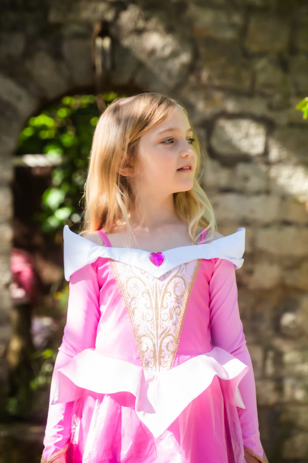 Girl standing in pink sleeping beauty inspired dress in front of brick background.