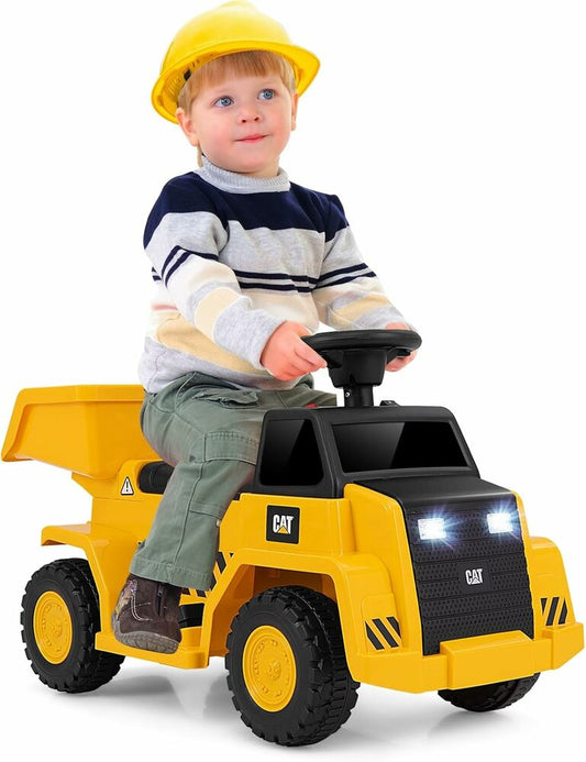 A child sitting on a yellow and black Caterpillar branded ride-on dump truck toy, wearing a hard hat.