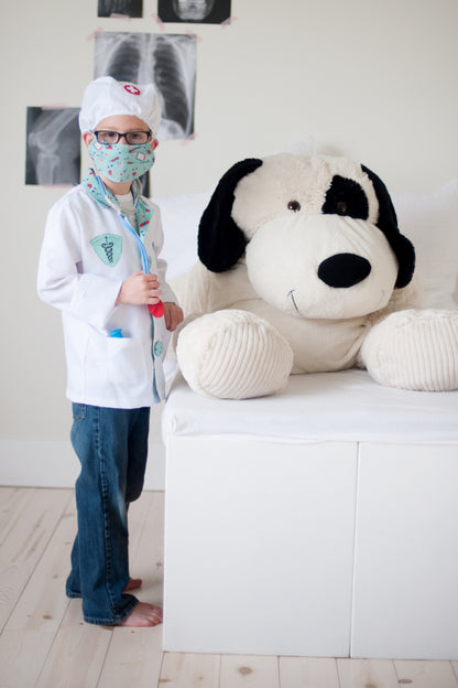 child in doctor costume standing by large stuffed dog.