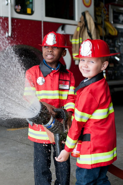 Two children dressed in red firefighter outfits with reflective tape details, playing with a water gun simulated as a fire extinguisher.
