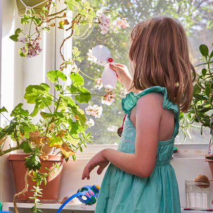 Child in a green dress watering plants by a window