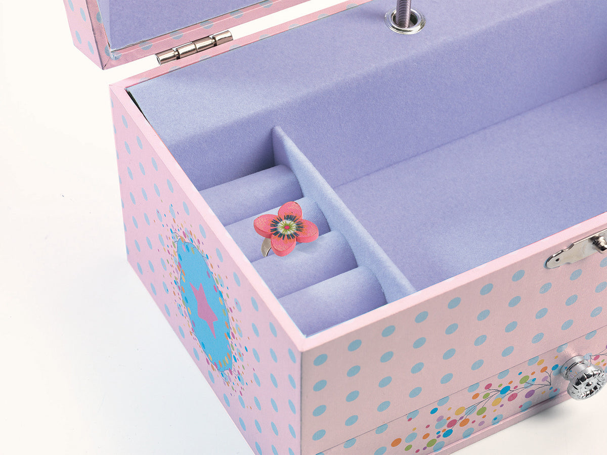 open, light pink wooden jewelry box patterned with light blue polka dots. The inside is lined with soft lavender felt, featuring a main open compartment, ring slots holding a small floral ring, and a silver keyhole on the outer edge.