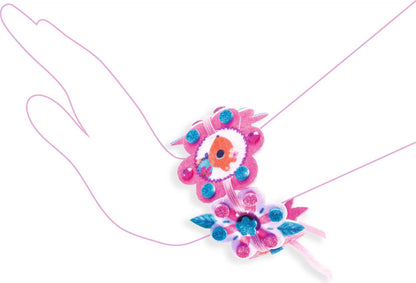A pink and blue floral wristband with pom-poms and bead details, shown on a white background with a faint hand outline.