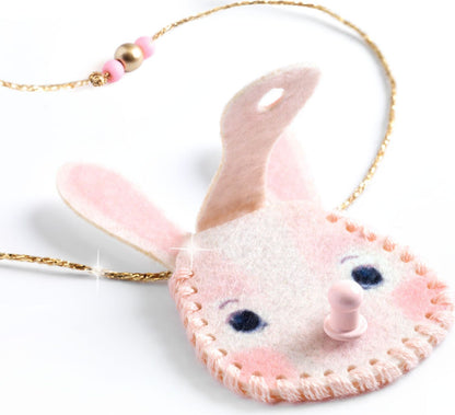 A pink felt bunny-shaped pendant necklace with embroidered details, a gold-tone chain, and pink and gold beads, shown on a white background.