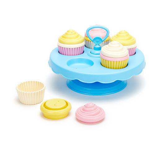 A light blue toy cupcake stands holding colorful to cupcakes, with a few loose cupcake pieces resting on the surface next to it.