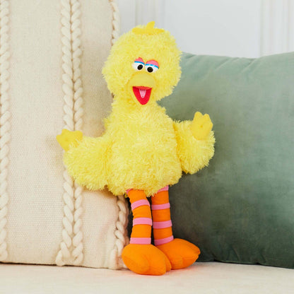 Yellow plush toy with orange feet and pink socks sitting on a couch.