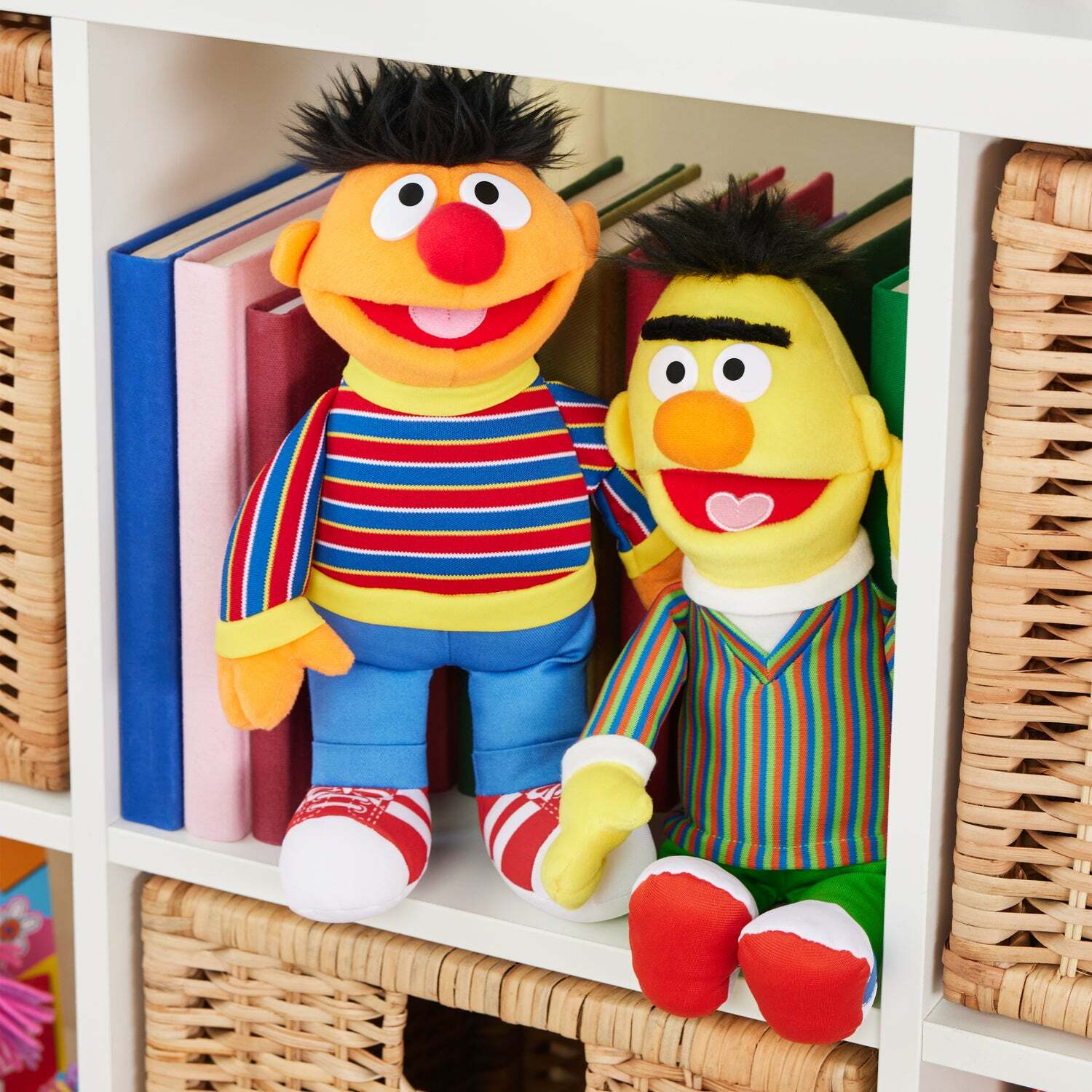 Ernie and Bert plush sitting on a white shelf with books behind them.