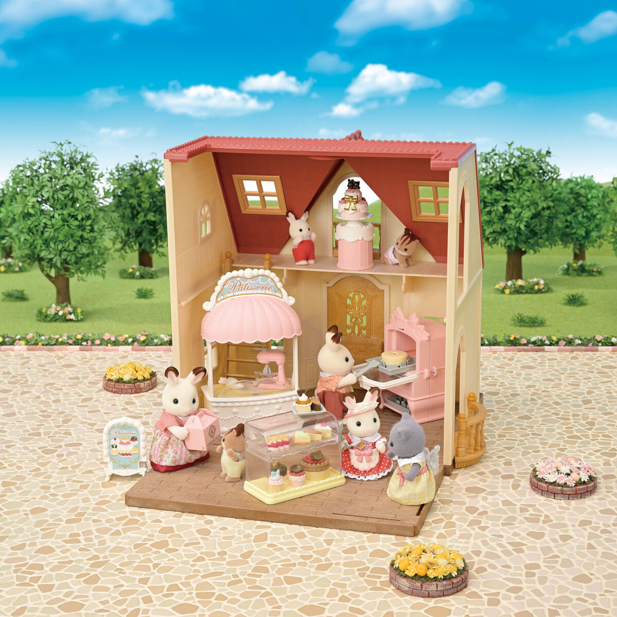 A Calico Critters Village Cake Shop Starter Set, including a cake shop with a pink and beige exterior, various cake decorations, a oven, and small figurines of animals wearing chef hats.