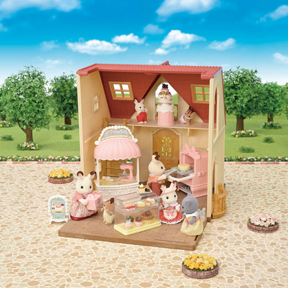 A Calico Critters Village Cake Shop Starter Set, including a cake shop with a pink and beige exterior, various cake decorations, a oven, and small figurines of animals wearing chef hats.