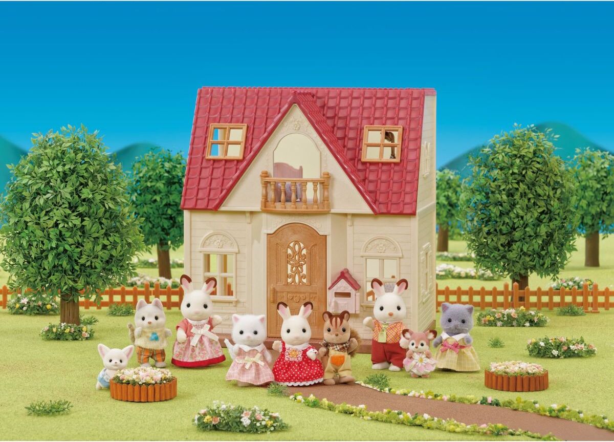 Toy house with toy animals in front on a grassy area with trees and mountains in the background