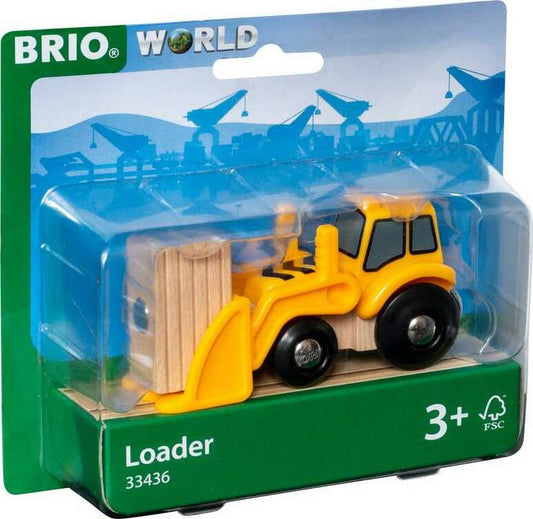 A BRIO World loader toy packaged in a clear plastic box with a green base, featuring a yellow and black loader with wooden elements. The packaging has illustrations of train tracks and a blue sky, with a label indicating the product is suitable for ages 3+ and made by Brio.
