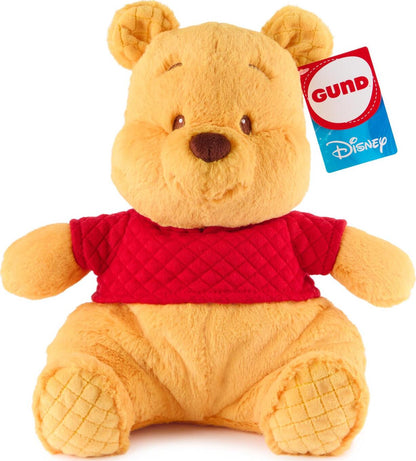 A plush toy of Winnie the Pooh, featuring a seated pose with a red t-shirt and soft pink plush nose. The toy appears cuddly and is slightly under-stuffed.