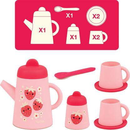 A children's play tea set shown with a matching instruction sheet above it. The set includes a pink teapot with a strawberry and flower print, a small bottle, a cup, a mug, a spoon, and matching saucers, all in soft pink and red tones.