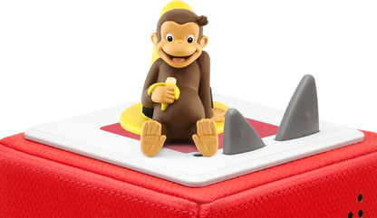 Curious George figurine holding a banana, seated on a yellow hat on a red tonie box.