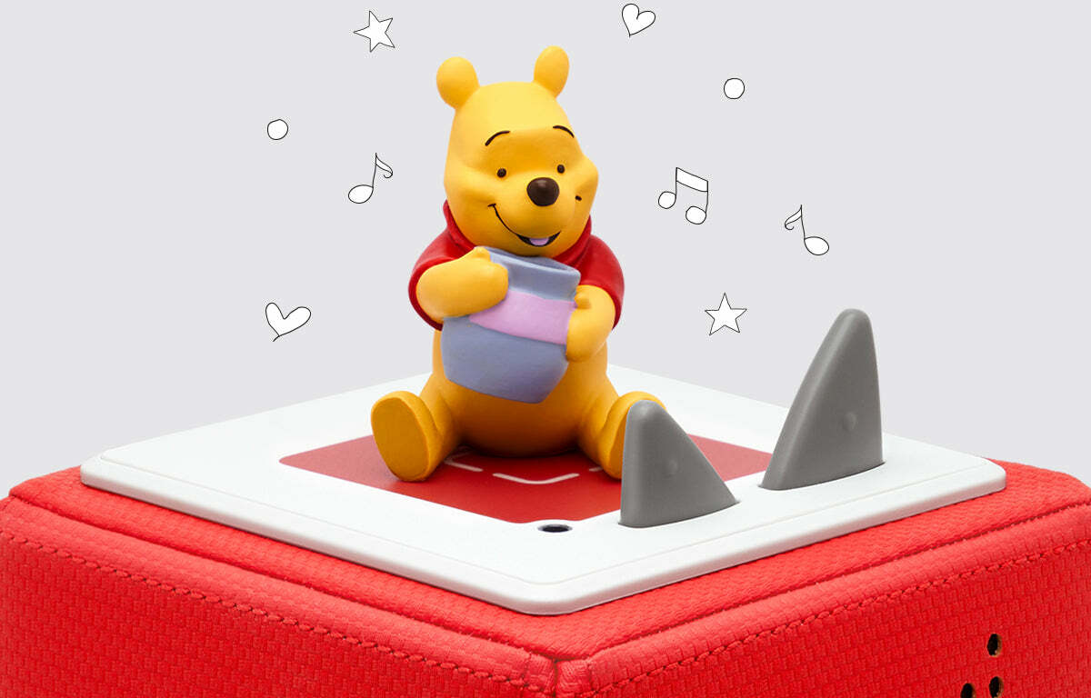 Winnie the pooh figurine sits on a red tonie box, holding a small pot, surrounded by floating illustrations of hearts, stars, and musical notes.