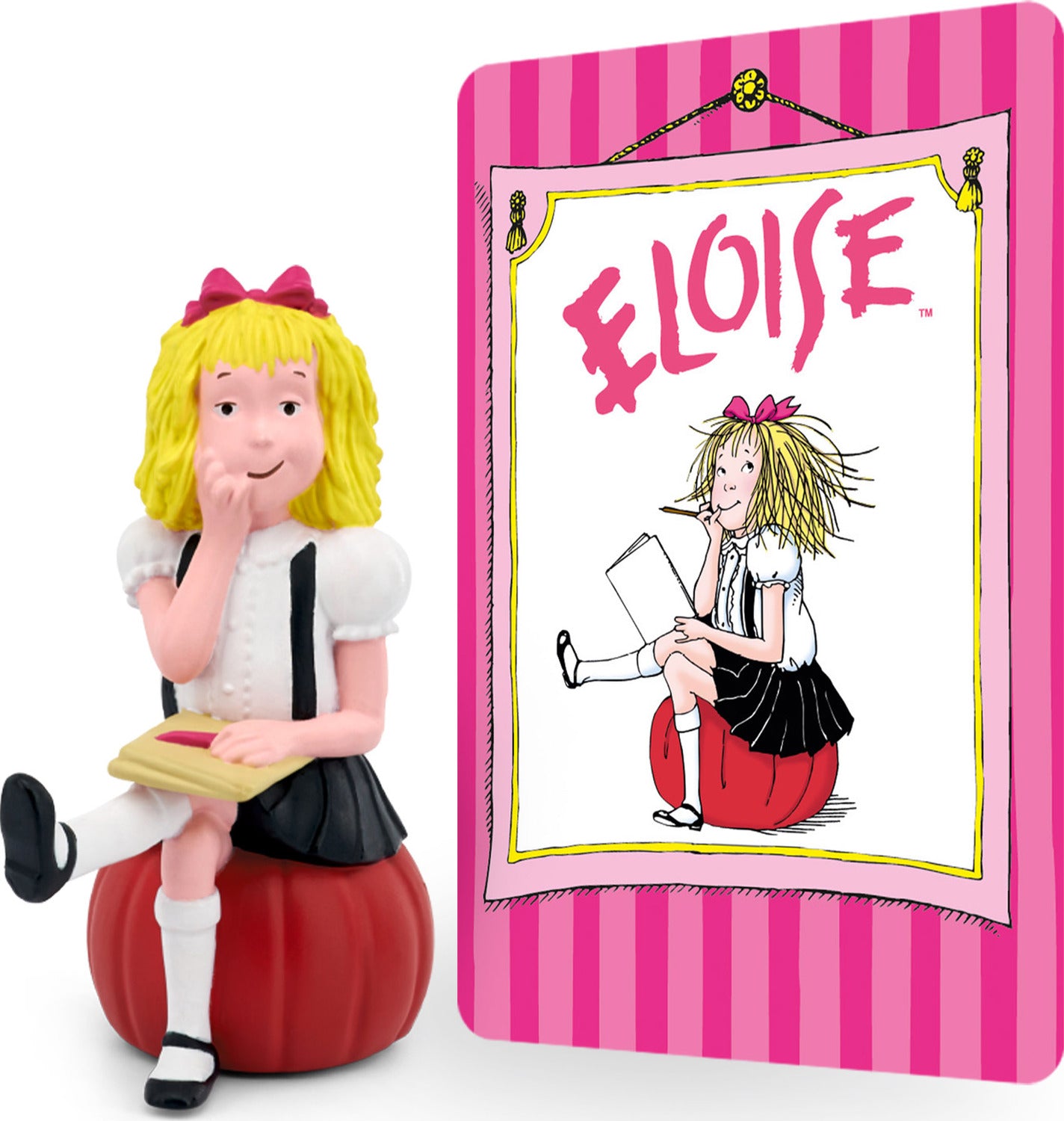 A figurine of a young girl with blonde hair sitting on a red apple, holding a book, next to a playback device, with a picture of the character 'Eloise' in a storybook format in the background.