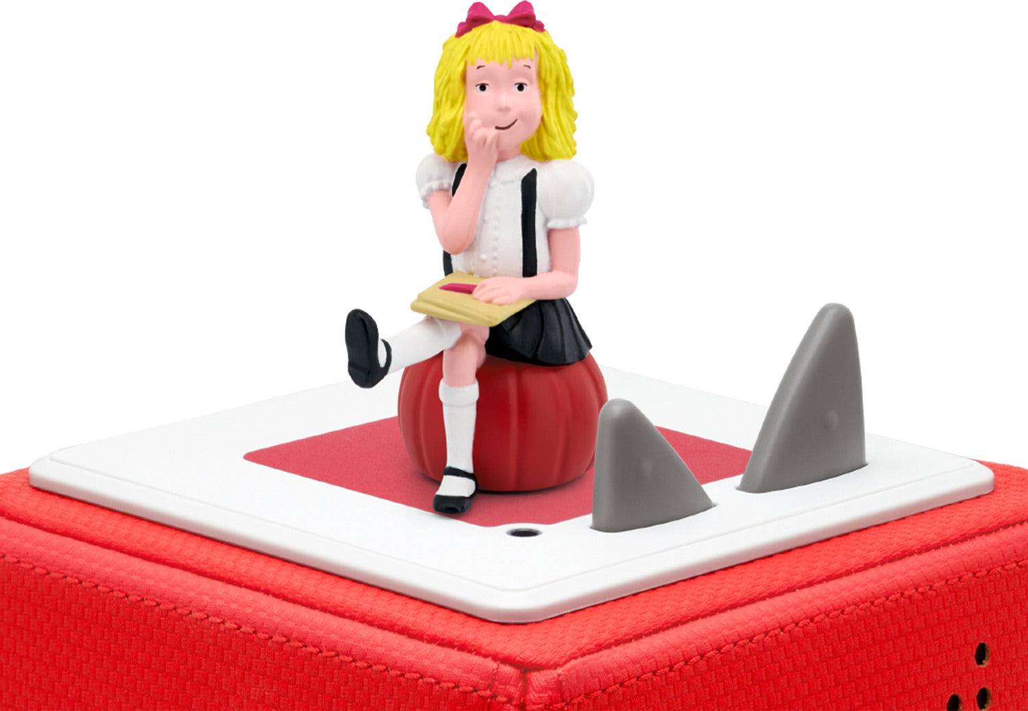 Elois blonde girl wearing a pink hair bow, a white shirt with black suspenders, and a black shirt seated on a red base holding a book.
on a tonie box.