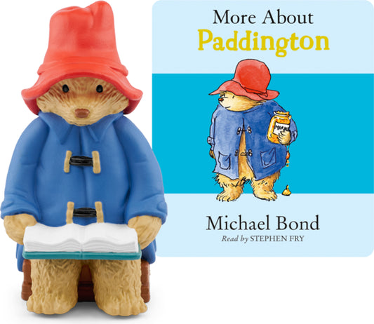 A figurine of Paddington Bear wearing his blue coat and red hat, holding a book, alongside a cover of the audiobook 'More About Paddington' featuring an illustration of Paddington and a young boy.