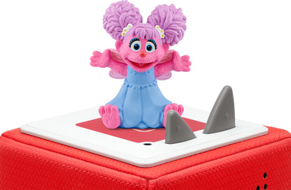 Abby Cadabby figurine with pink hair and blue outfit, sitting with arms open, on a red toniebox