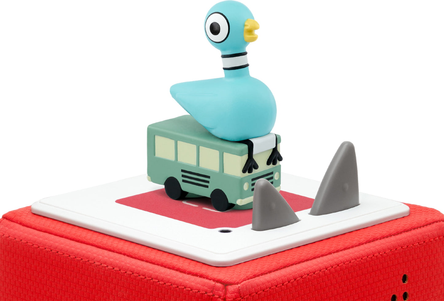 A figurine of a pigeon sitting on top of a toy bus with shark fin-shaped cutouts on the sides, on a red toniebox