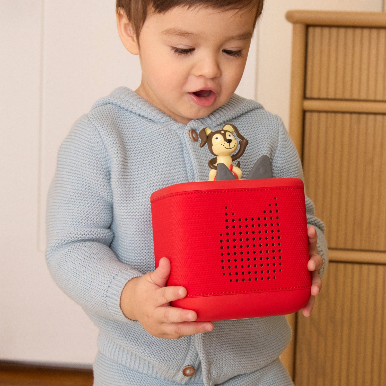 Child holding a red toy with a cartoon character on a light background